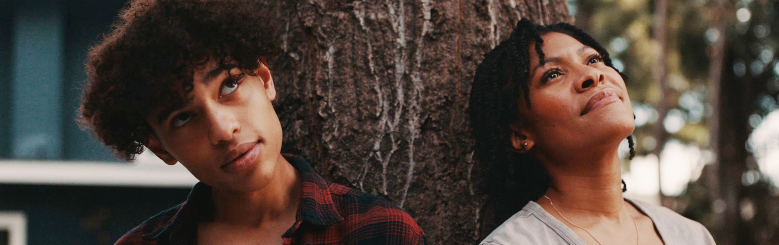 People leaning against a tree and smiling