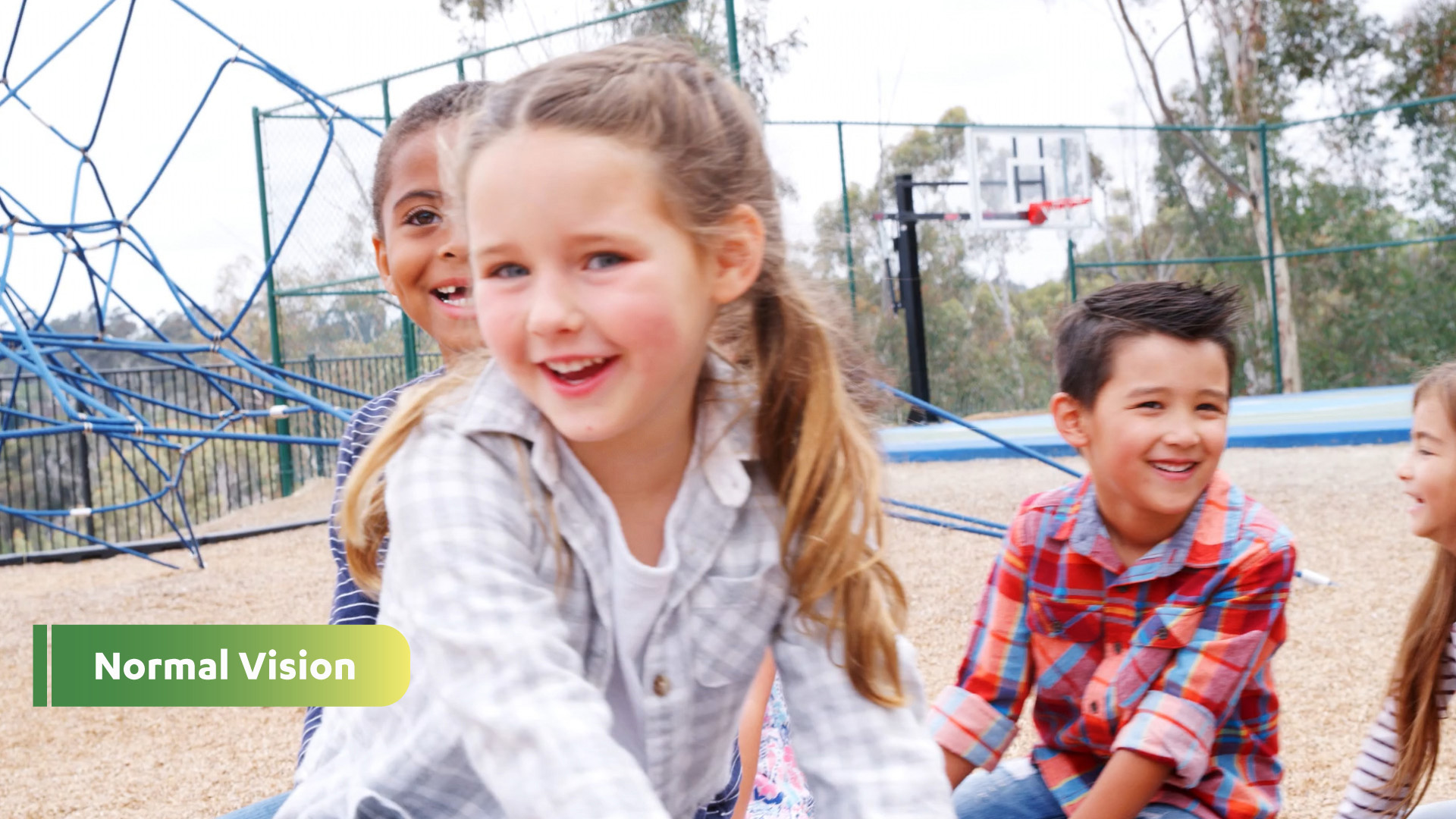Normal Vision: Photo of young girl in a gray checkered shirt smiling with other children on a playground.