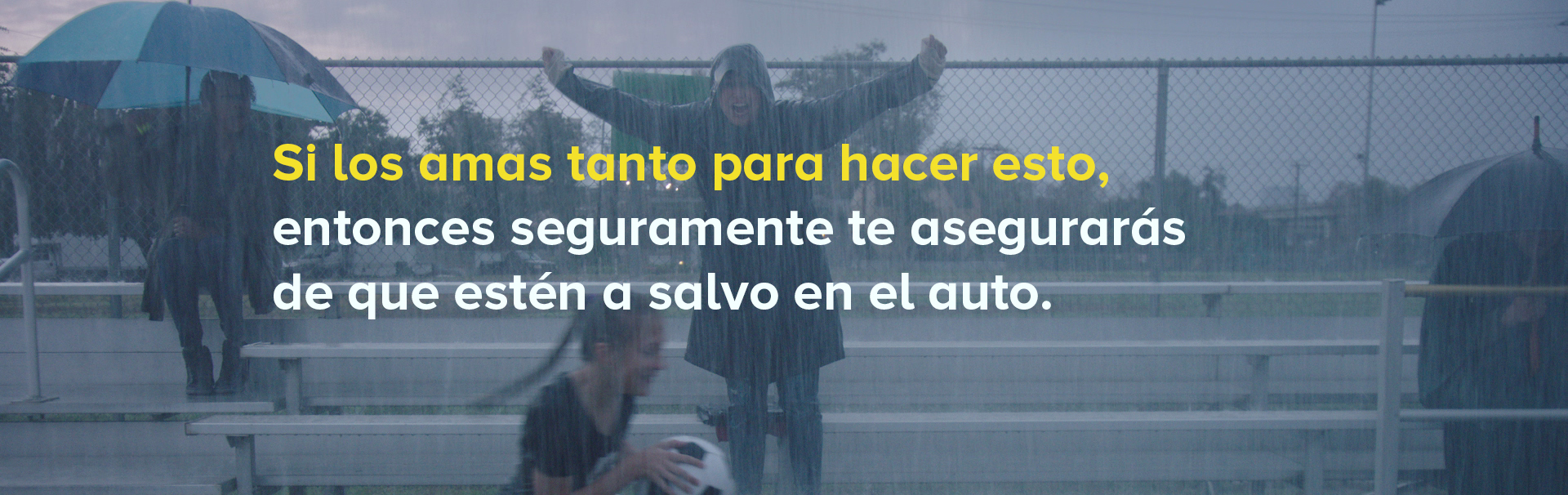 A woman wearing a raincoat stands up and cheers on some bleachers while it is pouring rain.