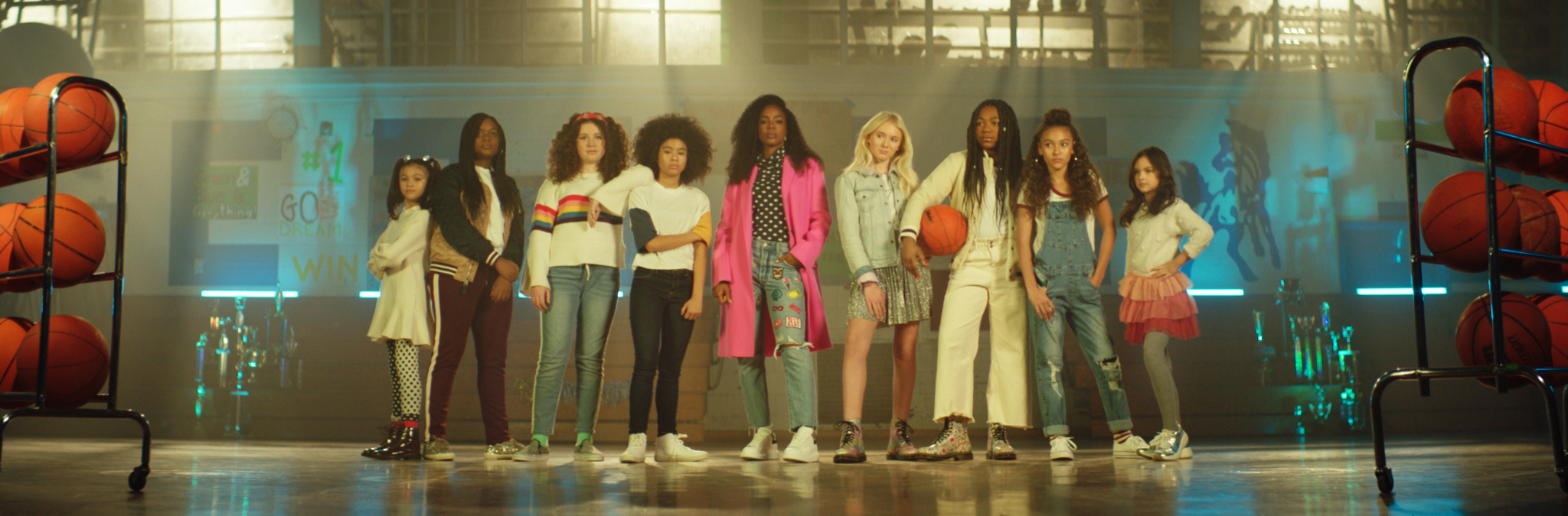 Ni&ntilde;as de pie en un gimnasio con pelotas de baloncesto.