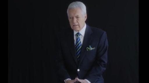 Alex Trebek sur une chaise dans une pièce noire.