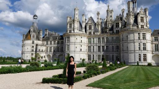 Woman stands outside a castle on a sunny day.