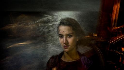 A girl stands on a boat at nighttime with the sea behind her.