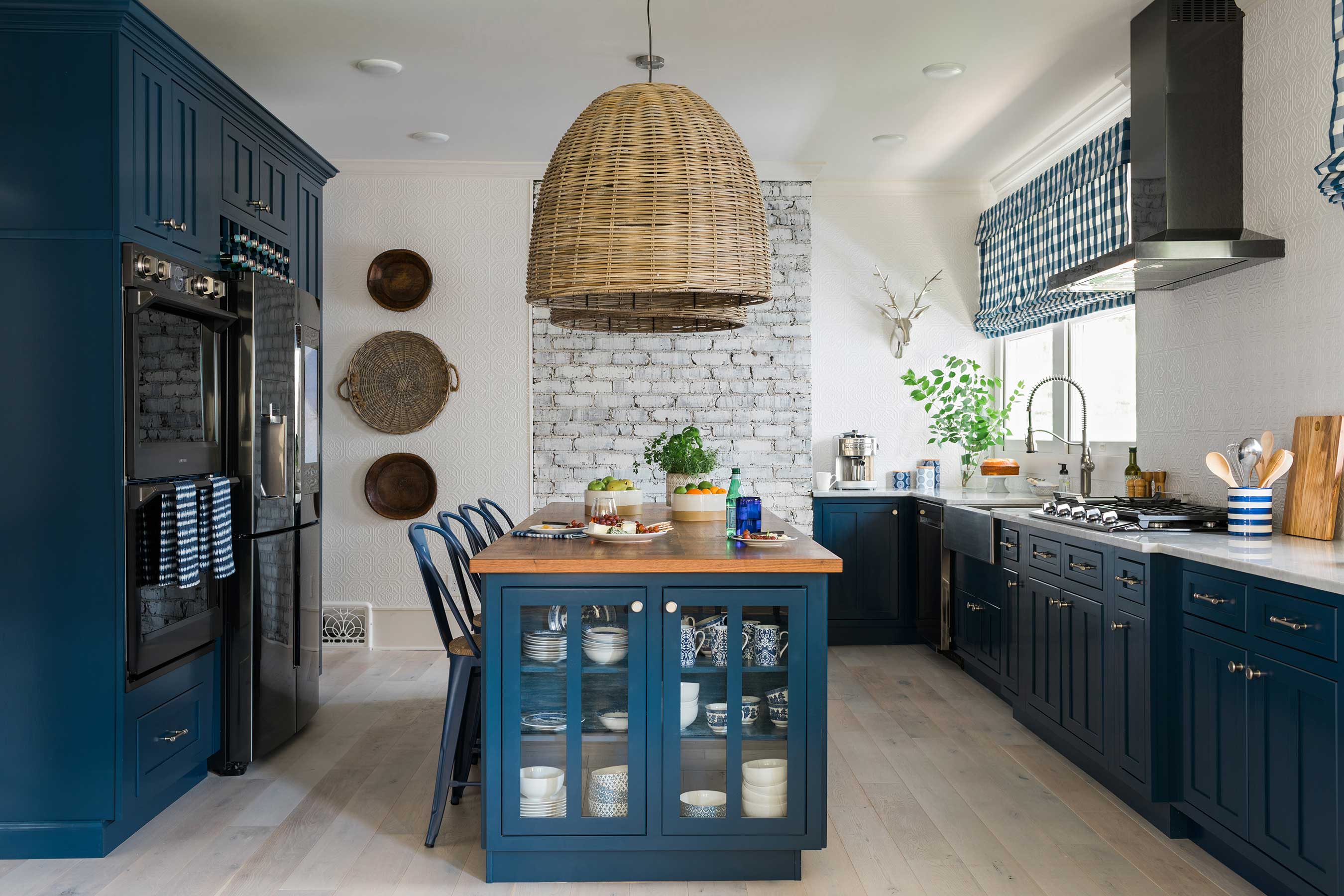 The kitchen of HGTV Urban Oasis 2017 utilizes key architectural elements and a subdued white and blue color scheme to achieve open-concept perfection. An exposed brick wall is whitewashed to serve as a stark backdrop, while bold navy blue cabinets and countertops in both white Carrara marble and black walnut continue the theme of clean, contrasting colors.