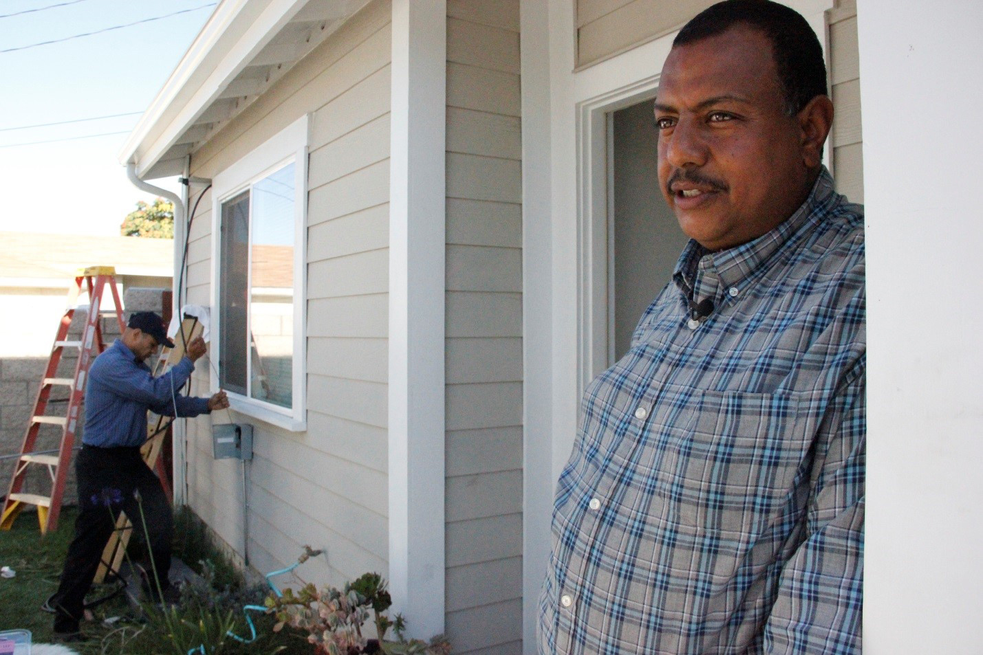 Habitat for Humanity homeowner Girmachew stands in the doorway of his Los Angeles home as a technician from Kahn Air installs a Carrier ductless home comfort system in his home. More than 150 Carrier ductless systems are being installed in Los Angeles as part of a donation of more than 500 systems donation to Habitat for Humanity this year.