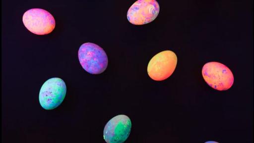 Various artificially brightly colored spotted eggs on a black background. The eggs look like they glow in the dark.