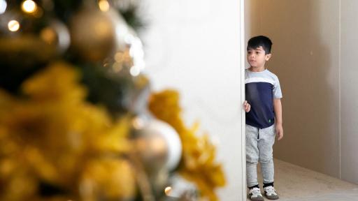 Boy looking around hallway corner at a festive tree