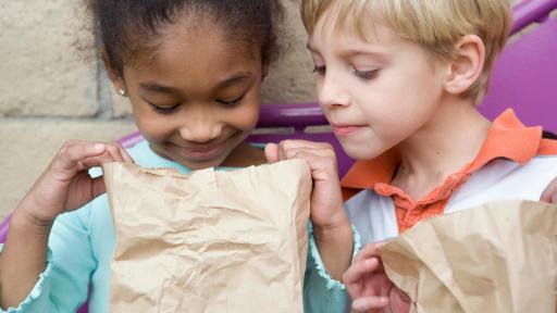 Girl and boy look into a brown paper bagged lunch
