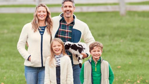 Family wearing Lands Ends Sherpa outerwear, standing outside with baby sheep nearby