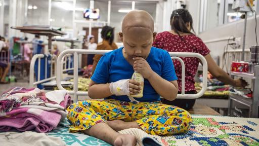 Child with scar across bald head, sitting on bed in the hospital