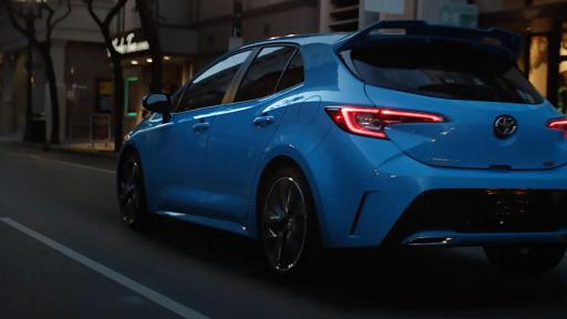 The back of a blue 2019 Toyota Corolla Hatchback driving down a road.