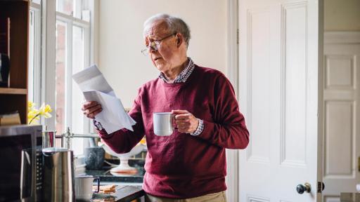 Older man reading some paper and drinking tea.