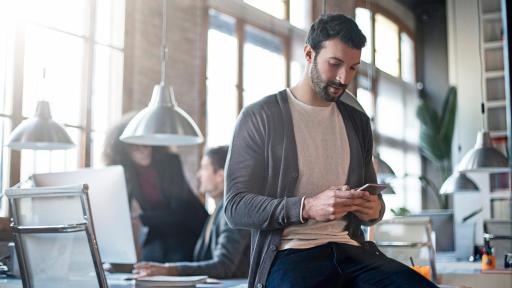 Man sitting on a desk, looking at his phone