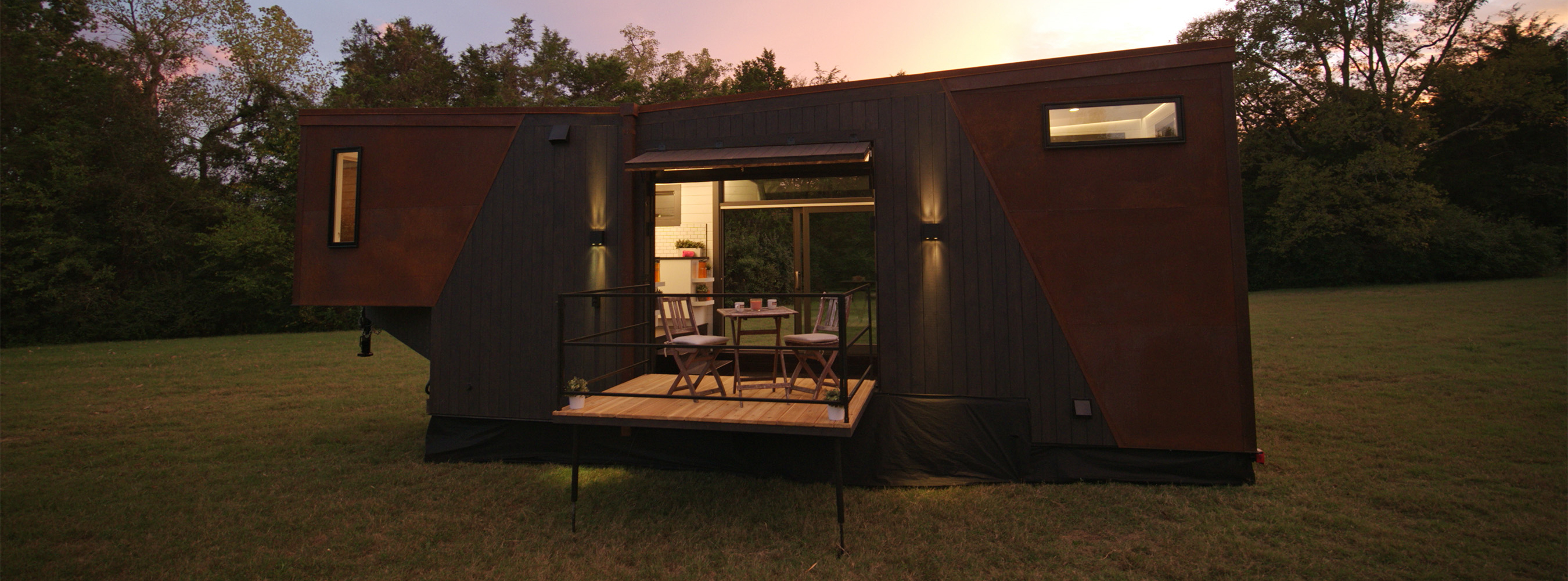 Image of a tiny house with a very modern aesthetic, located in a green field surrounded by trees.