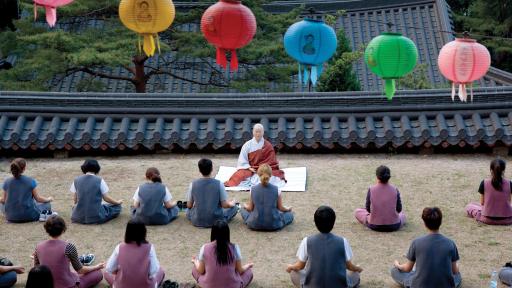 Meditators sitting outdoors, colorful paper lamps sit above them.
