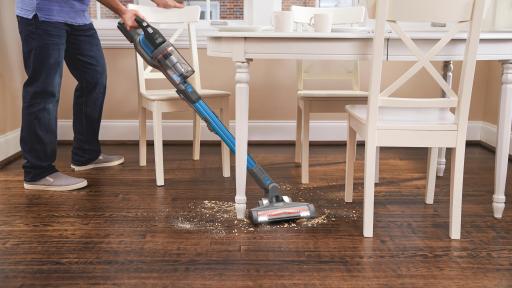 Cordless vacuum sweeping between a kitchen table and chairs.