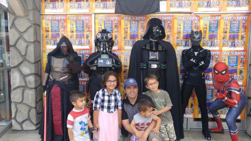 A family posing with comic book characters in front of posters.