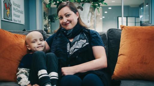 A mother sits on a couch with her son who is bald from chemotherapy.