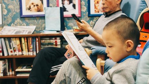 An older man and a young child sitting in a room reading books.