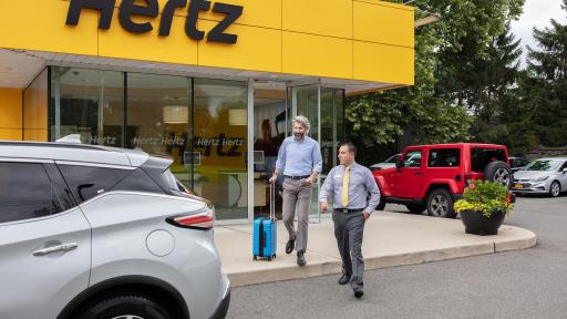 Two men walking to a Hertz Rent a car.
