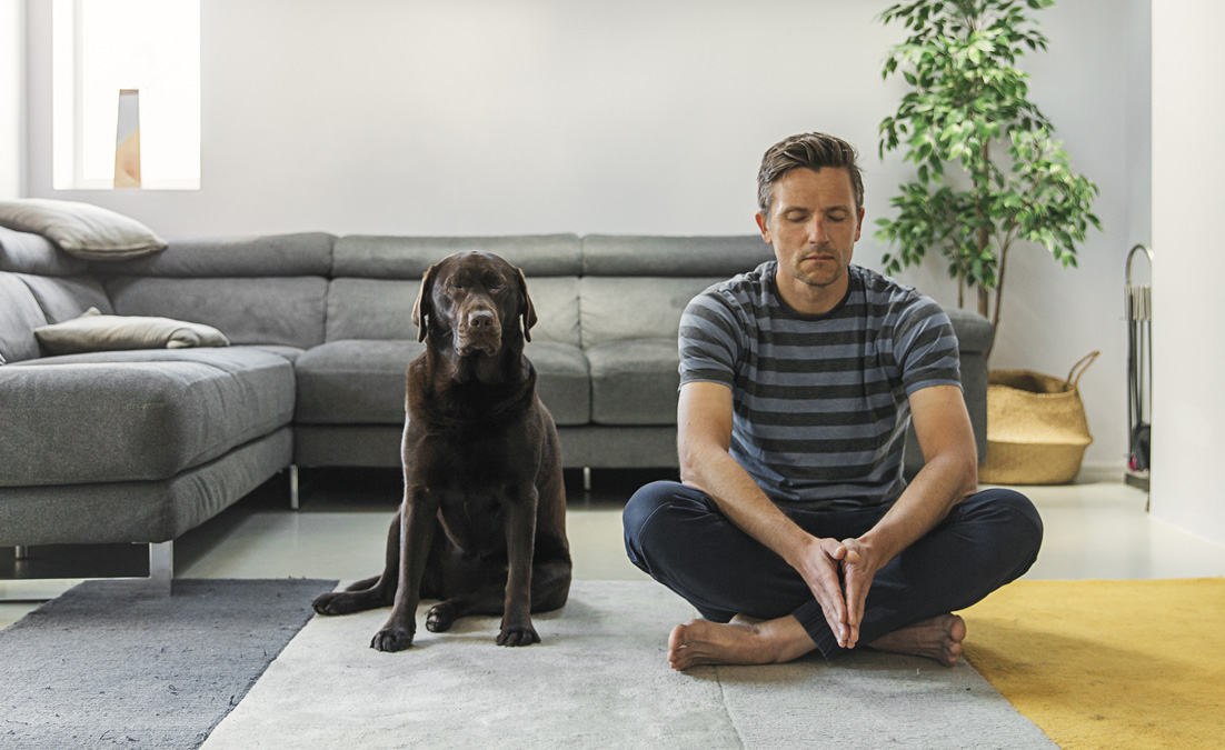 Man and dog sitting on living room floor in meditation