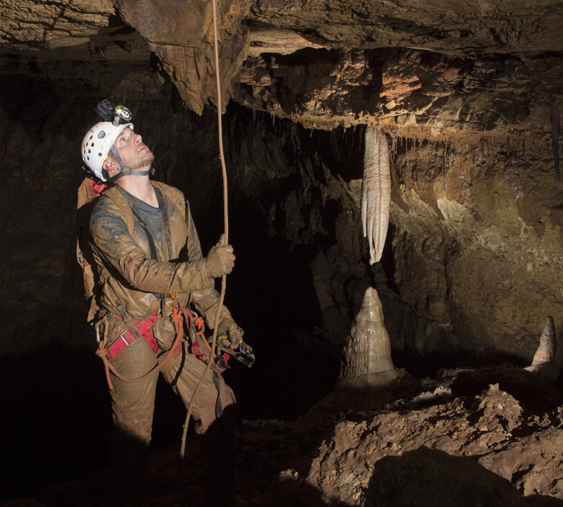 Man in helmet and head lamp looking up towards a stalactite