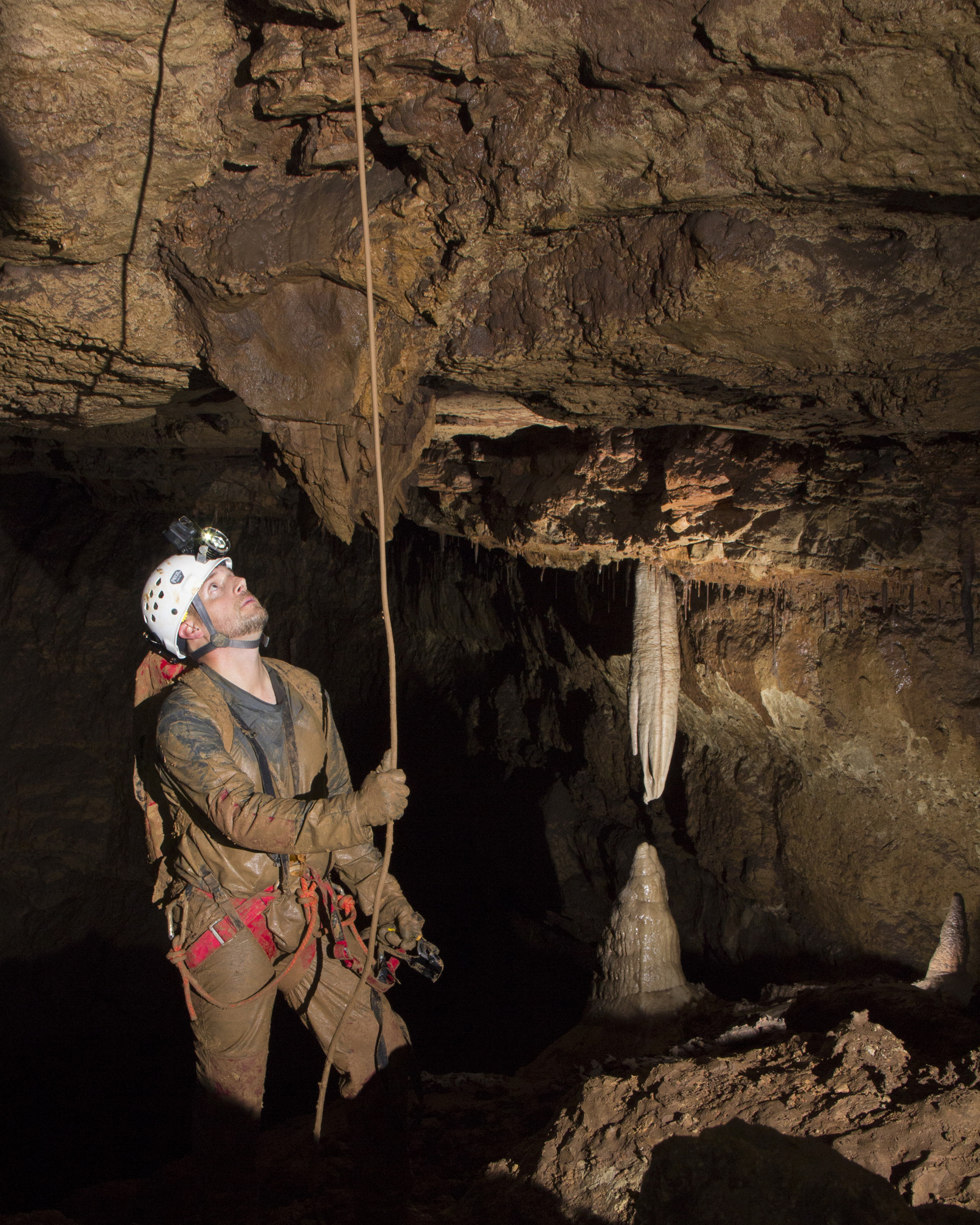 Man in helmet and head lamp looking up towards a stalactite