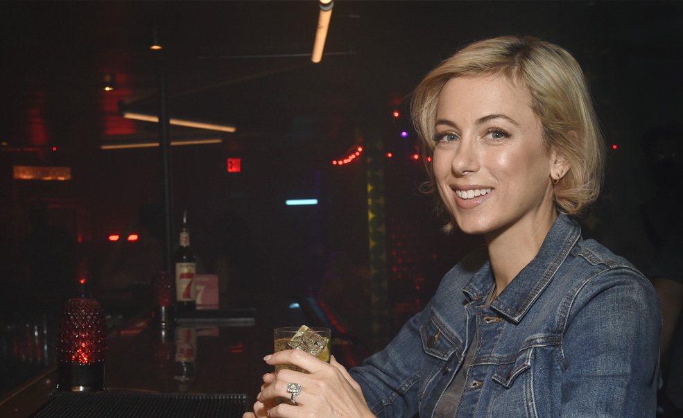 Photo of Iliza Shlesinger in a bar holding a bottle.