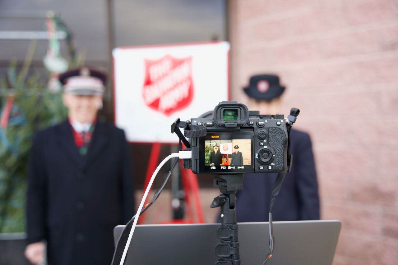 Camera shot of Commissioners Kenneth and Jolene Hodder standing next to a Salvation Army Red Kettle Camera shot of Commissioners Kenneth and Jolene Hodder standing next to a Salvation Army Red Kettle