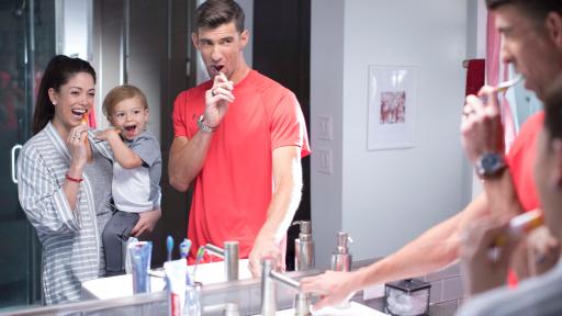 Michael Phelps and family are brushing their teeth while looking into the bathroom mirror.