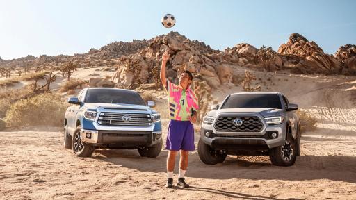 Campos throwing a soccer ball standing in front of two Toyota trucks.