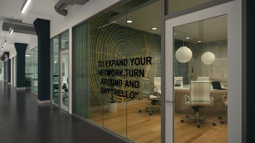 A meeting room with wood floor as seen through its glass wall and door from the hallway.
