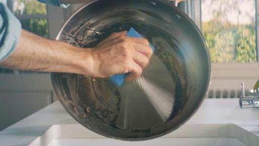 Man cleans pan with scrunge sponge