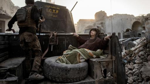 An elderly woman is driven through the city on the back of a Humvee
